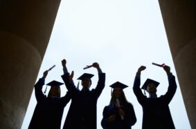 Male and female graduates in cap and gown raising their diplomas in celebration