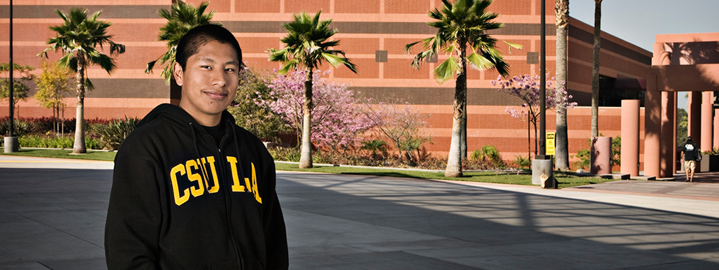 Latino student wearing CSU Los Angeles sweater standing in front of campus