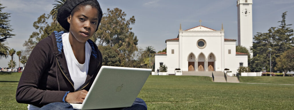 African American female student sitting on the lawn working on her laptop