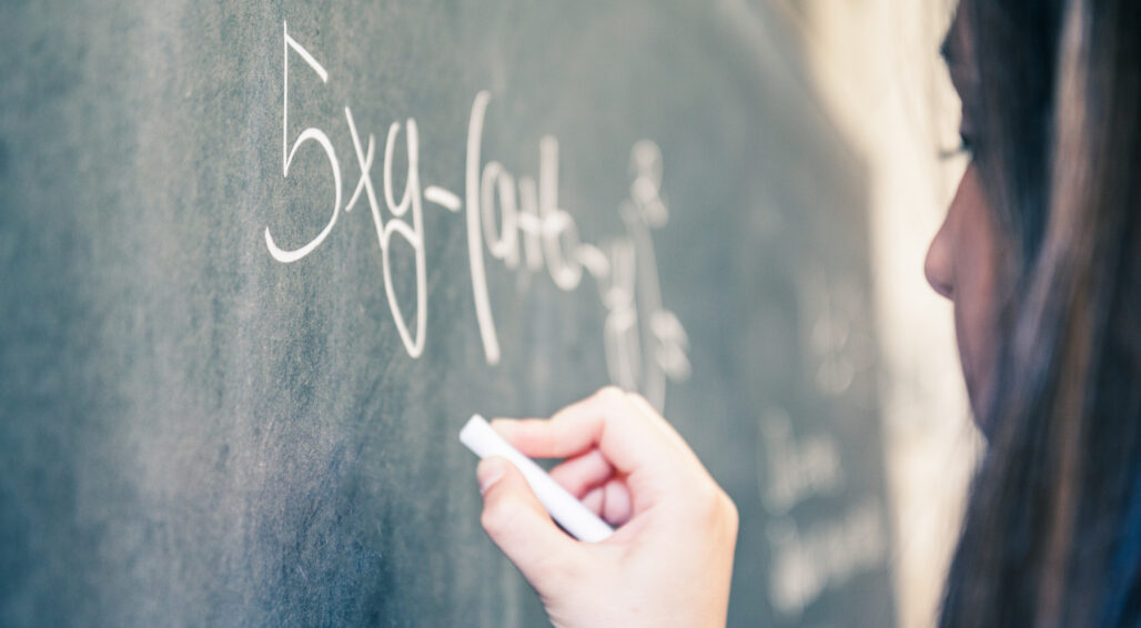 Teenage student working on math equation at blackboard