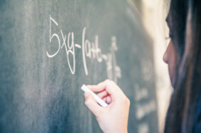 Teenage student working on math equation at blackboard