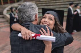 A happy student, holding a diploma, hugs her father