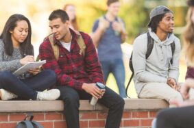 Students sitting on brick ledge looking at notes and socializing