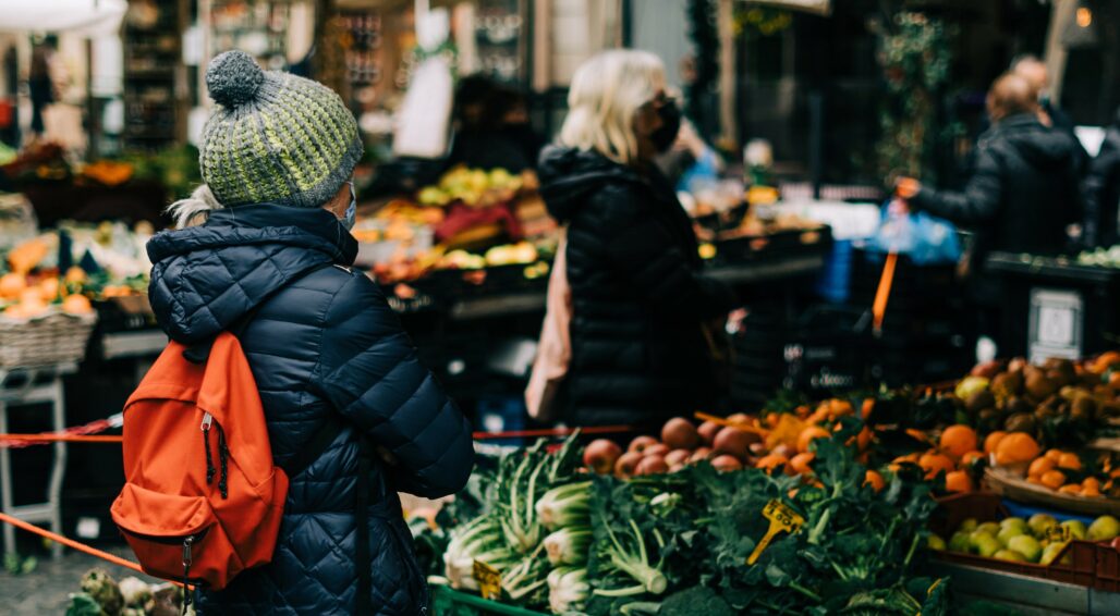 Female student in winter clothes standing in front of fresh produce stall